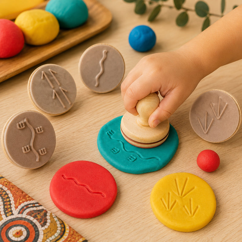 Child using Educational Colours Indigenous Australian animal track dough stamps with colourful modelling dough on a wooden table during sensory learning play. The image shows tactile impressions of Indigenous inspired animal track symbols created in dough using easy grip wooden handled stamps.
