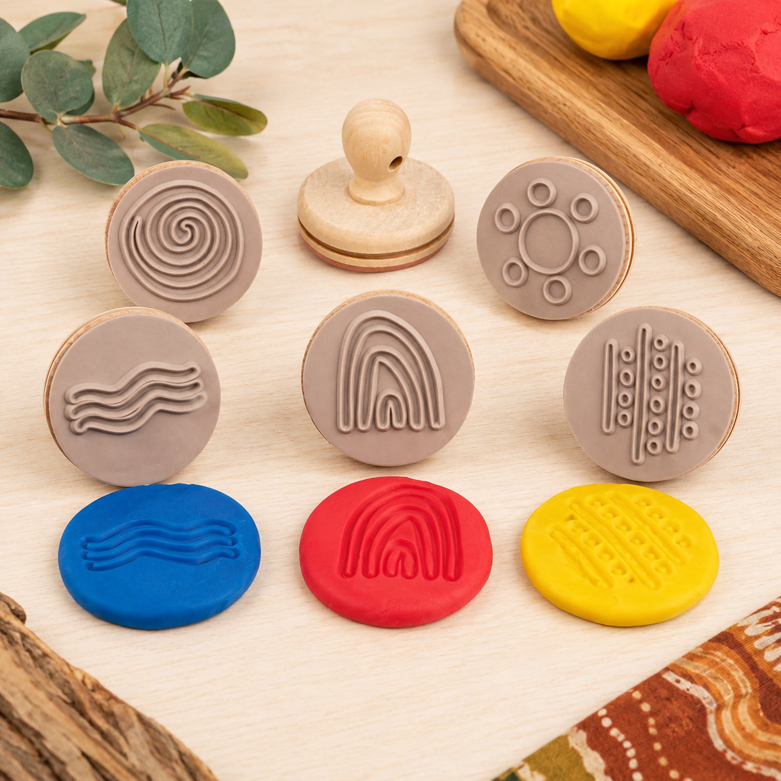 Educational Colours Wooden Dough Stamps Indigenous Australian Nature Symbols set arranged on a wooden table with colourful dough impressions. The image displays nature inspired symbol stamps including rainbow, waterhole, smoke and rain patterns designed for sensory learning and creative play.