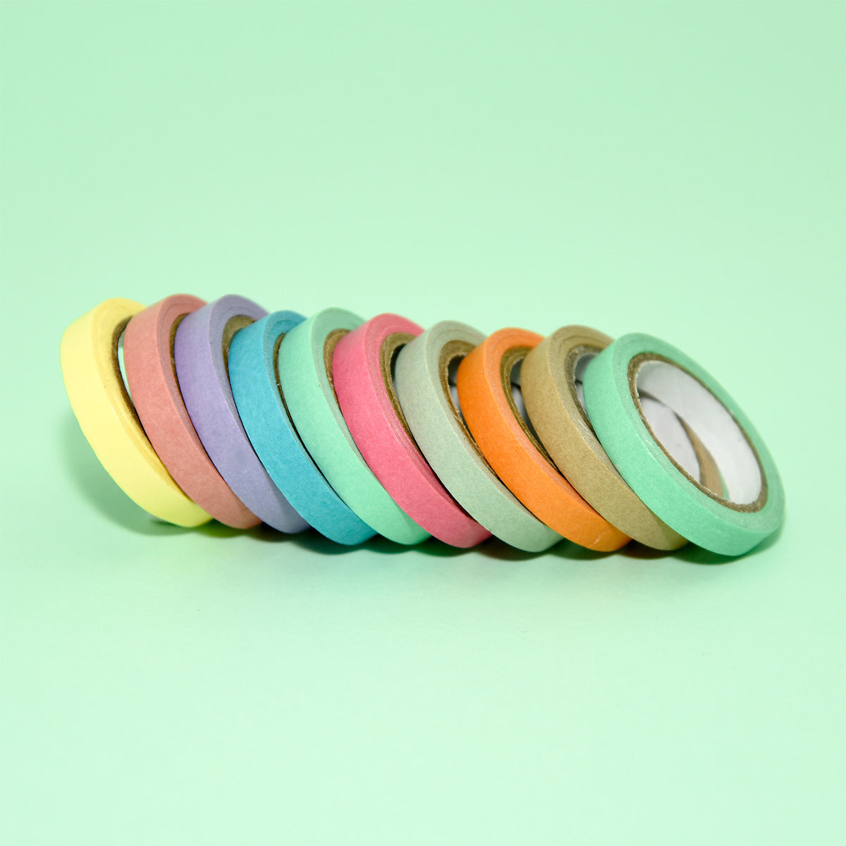 Ten slim deco tape rolls lined up in a row on a mint green background