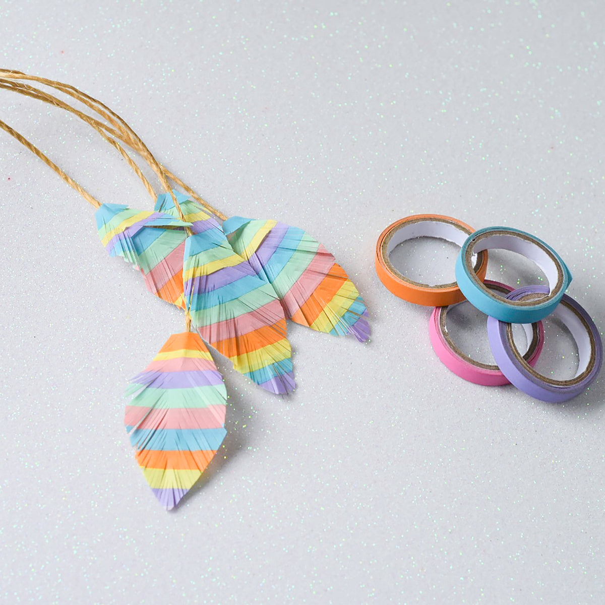 Striped paper leaves made from layered pastel tape hanging on gold twine beside loose rolls