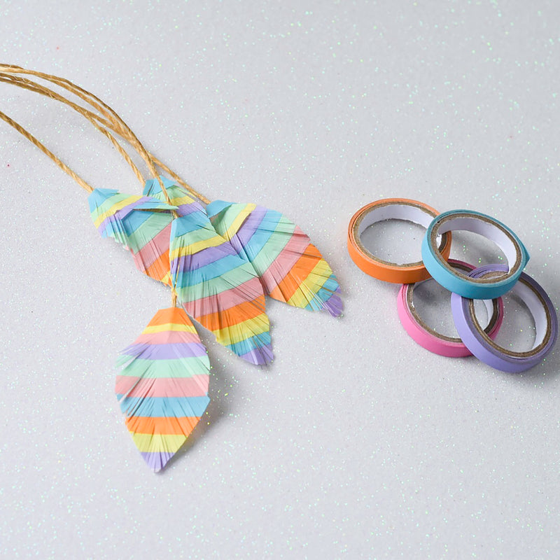 Striped paper leaves made from layered pastel tape hanging on gold twine beside loose rolls