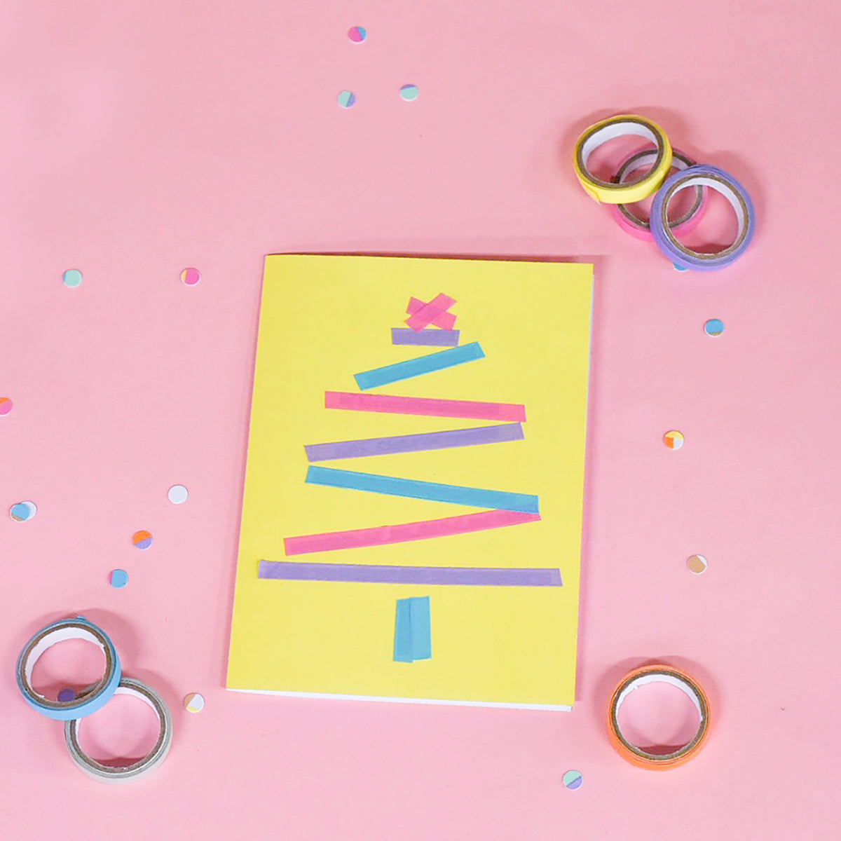 Yellow card with a Christmas tree built from pastel tape strips, loose rolls and confetti on a pink surface