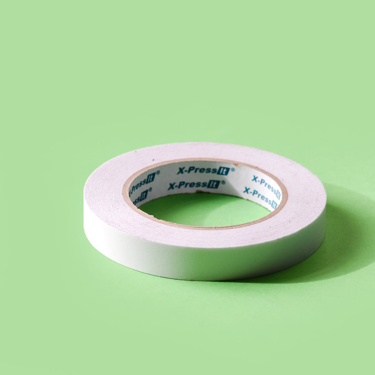 White X-Press It double sided tape roll on its side with branded core on a green background
