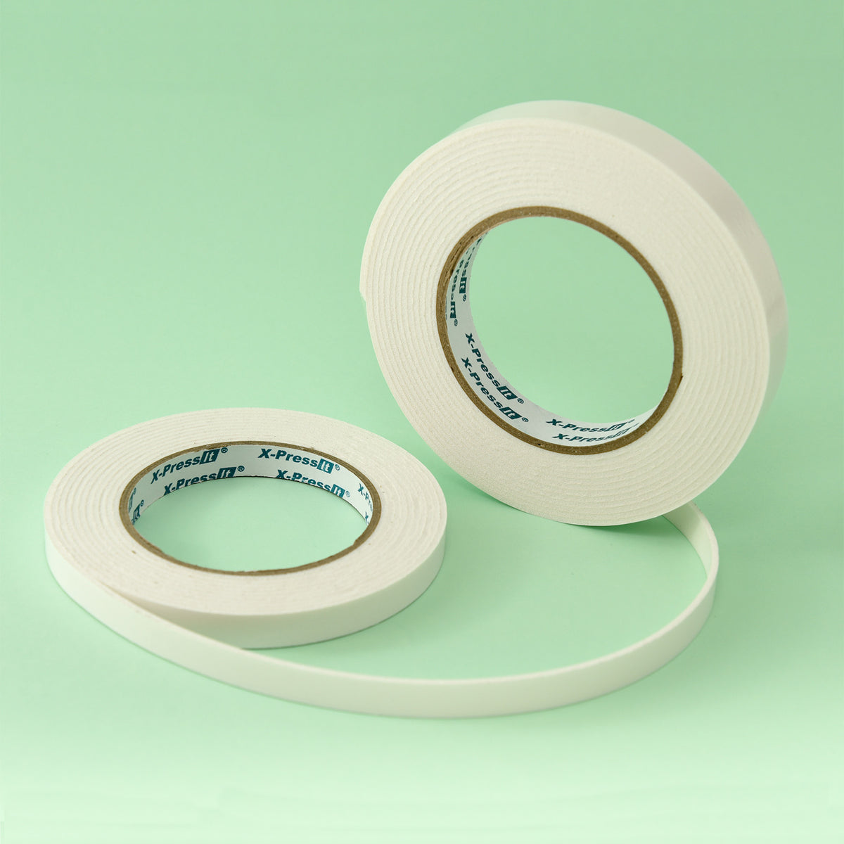 Two white X-Press It foam mounting tape rolls in different widths on a mint green background