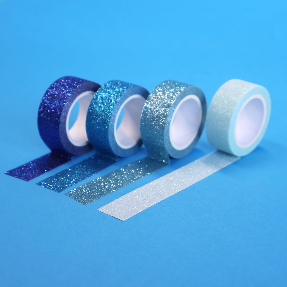 Four X-Press It blue glitter tape rolls from royal blue to pale aqua with strips unrolled on blue
