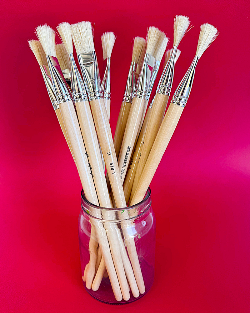 Assorted X-Press It hog hair flat and round brushes standing in a glass jar on a crimson red background