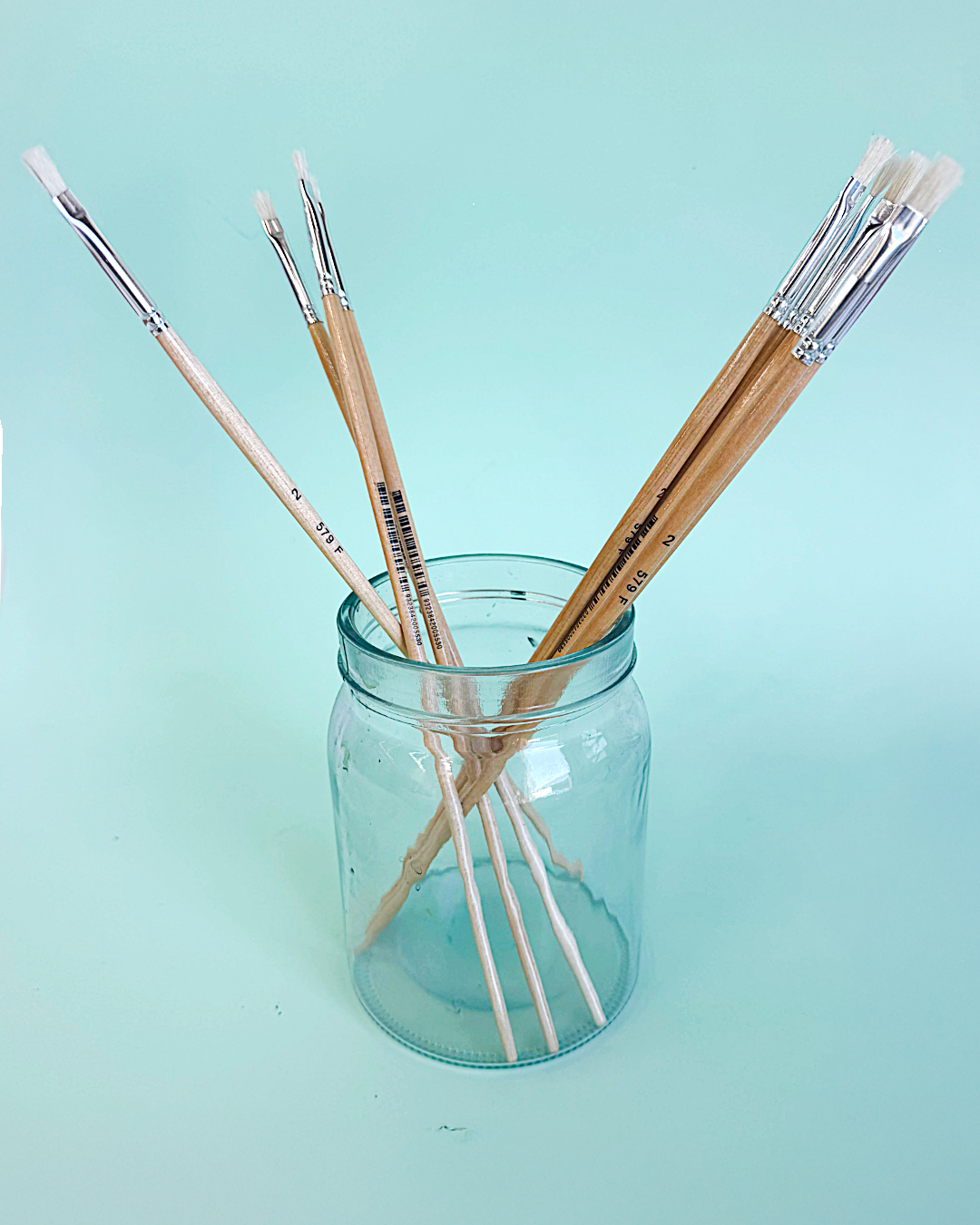 Assorted X-Press It hog hair flat and round brushes standing in a glass jar on a mint green background
