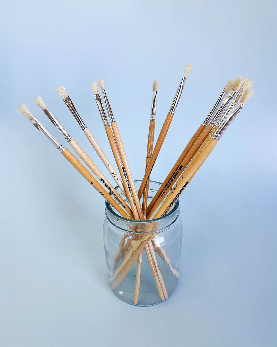 Assorted X-Press It hog hair flat and round brushes standing in a glass jar on a pale blue grey background