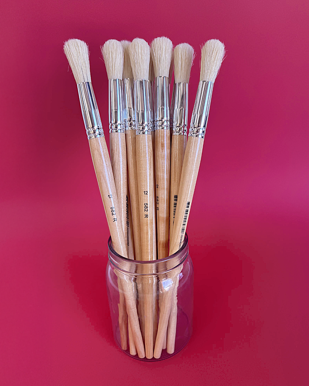 Glass jar of X-Press It size 12 hog hair round brushes with full cream heads against a deep red background