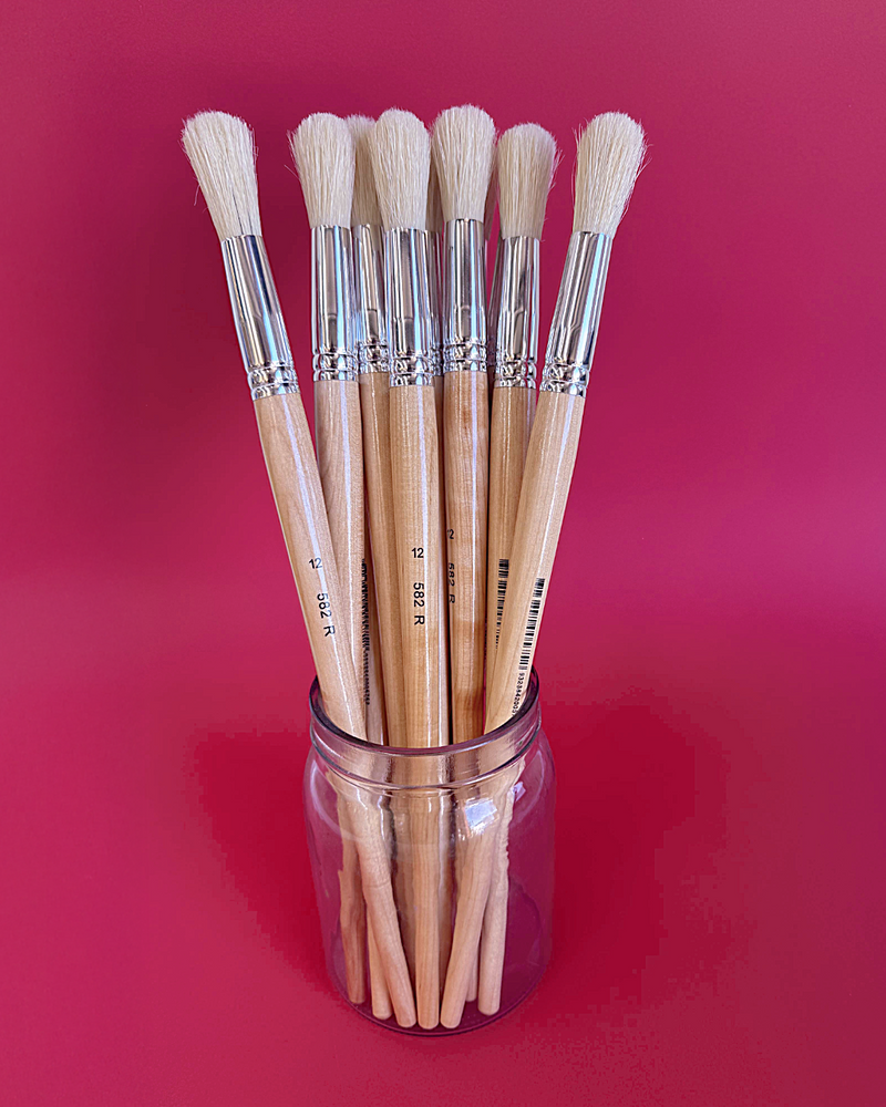 Glass jar of X-Press It size 12 hog hair round brushes with full cream heads against a deep red background