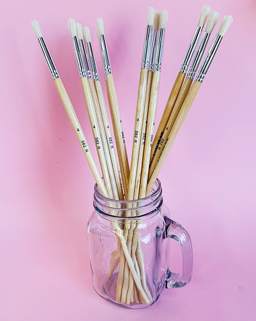 Mason jar holding a bundle of X-Press It size 4 hog hair round brushes, set against a pale pink backdrop