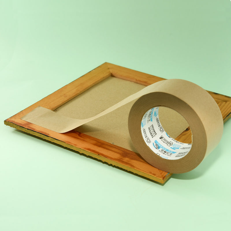 Brown kraft tape roll sealing the back edge of a timber picture frame on a pale green background