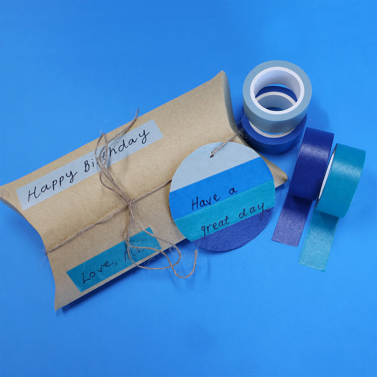 Kraft pillow box tied with twine, decorated with blue tape strips and a handwritten Happy Birthday message, beside Ocean rolls