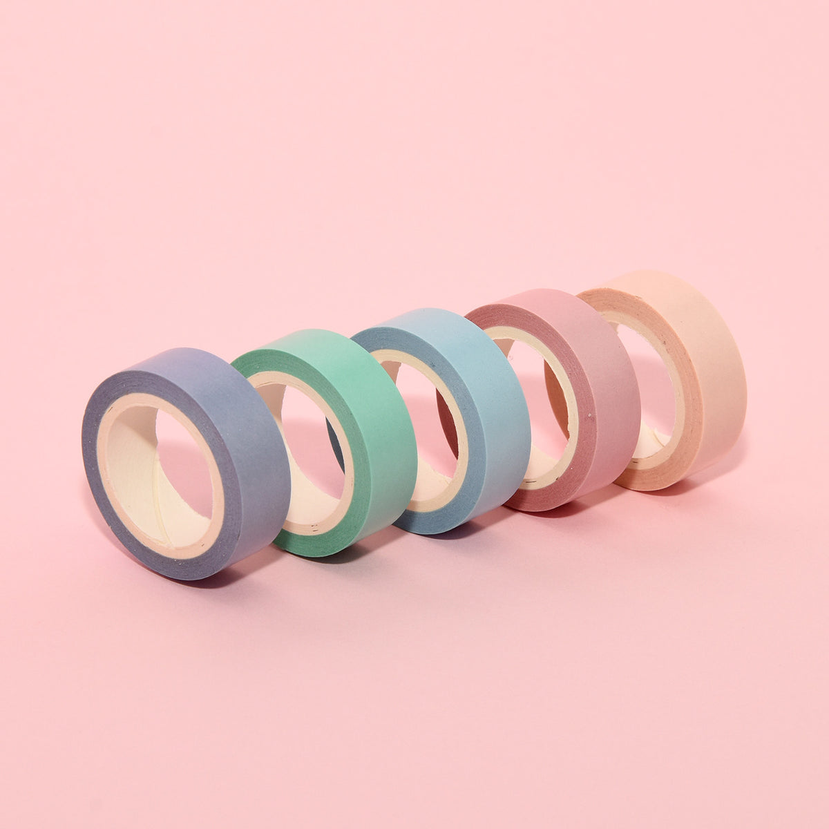 Five pastel paper deco tape rolls standing in a row on a pink background: lilac, mint, blue, pink and peach