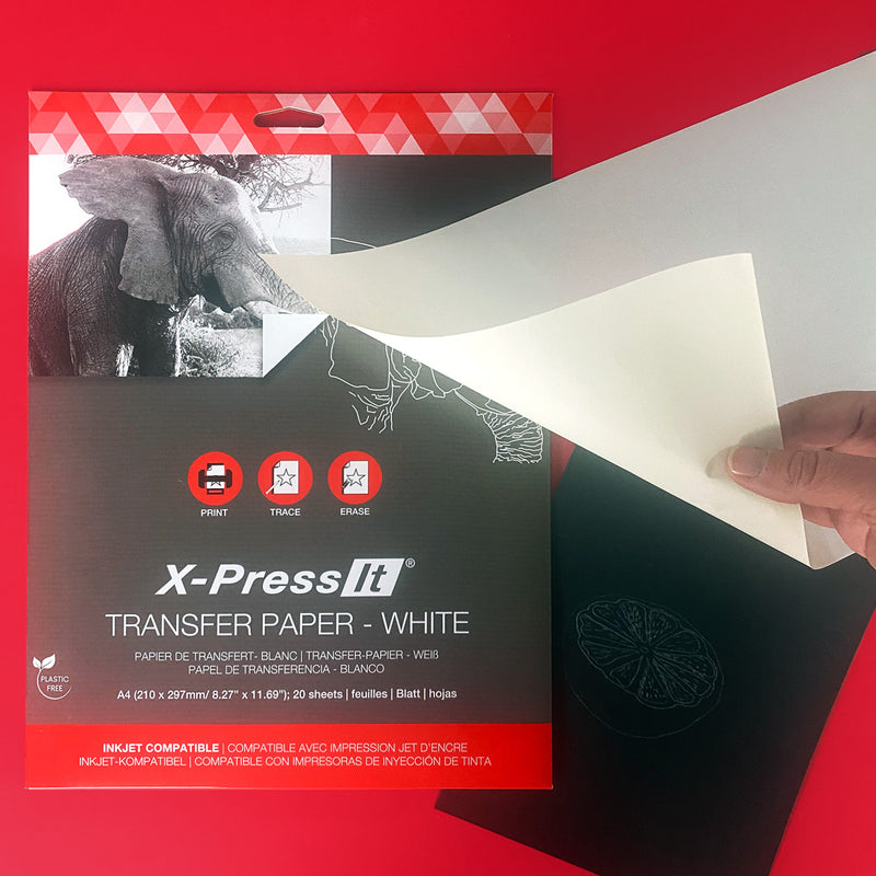 Hand lifting an X-Press It White transfer sheet to reveal white traced lines on black paper, pack front on a red background