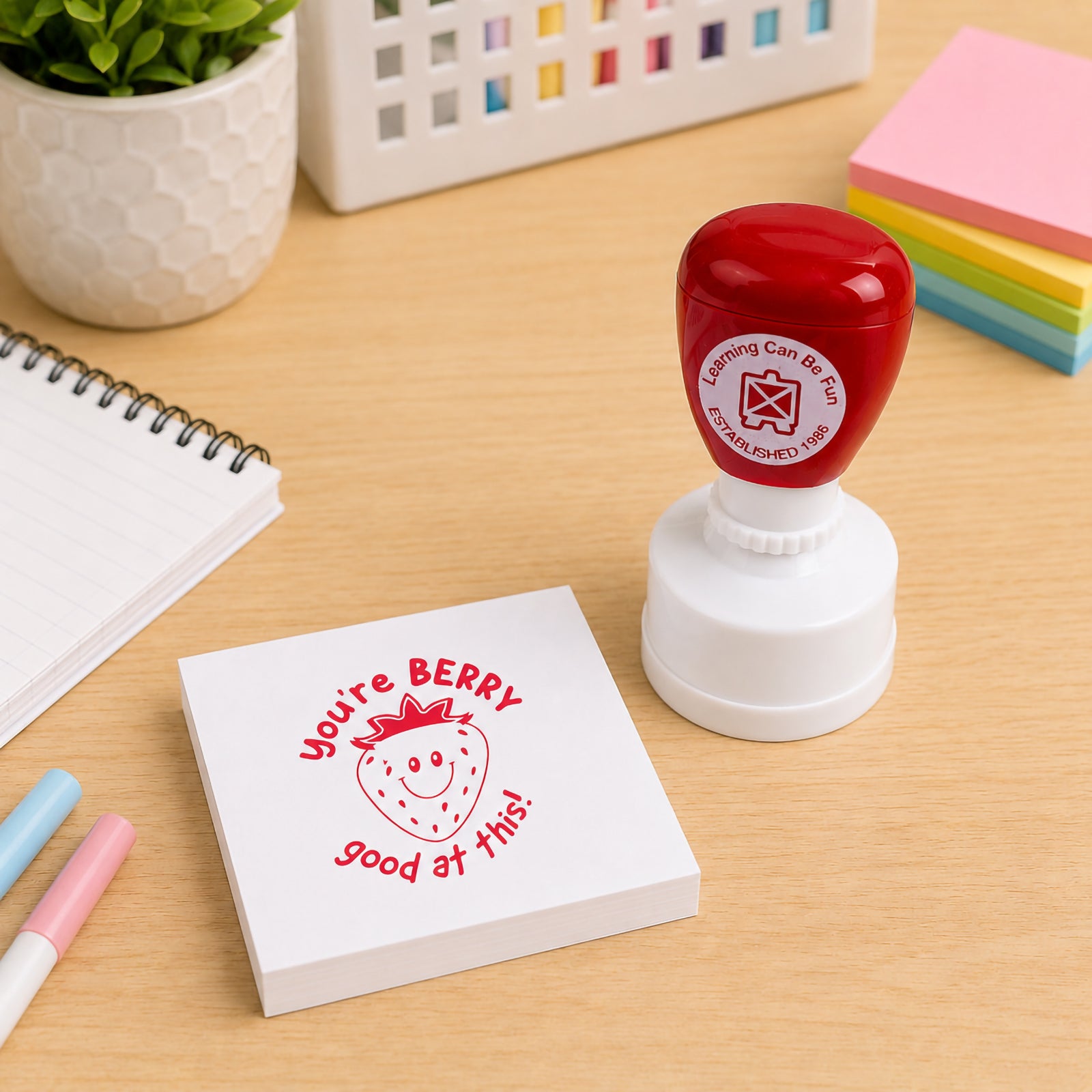 The You're Berry Good At This Merit Stamp displayed with sticky notes, notebooks and classroom stationery. The vibrant red stamp impression demonstrates how teachers can provide engaging and memorable feedback that motivates students.