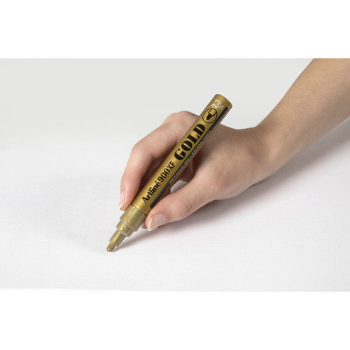 Artline 900 gold metallic marker writing on black surface showing full opacity and reflective finish
