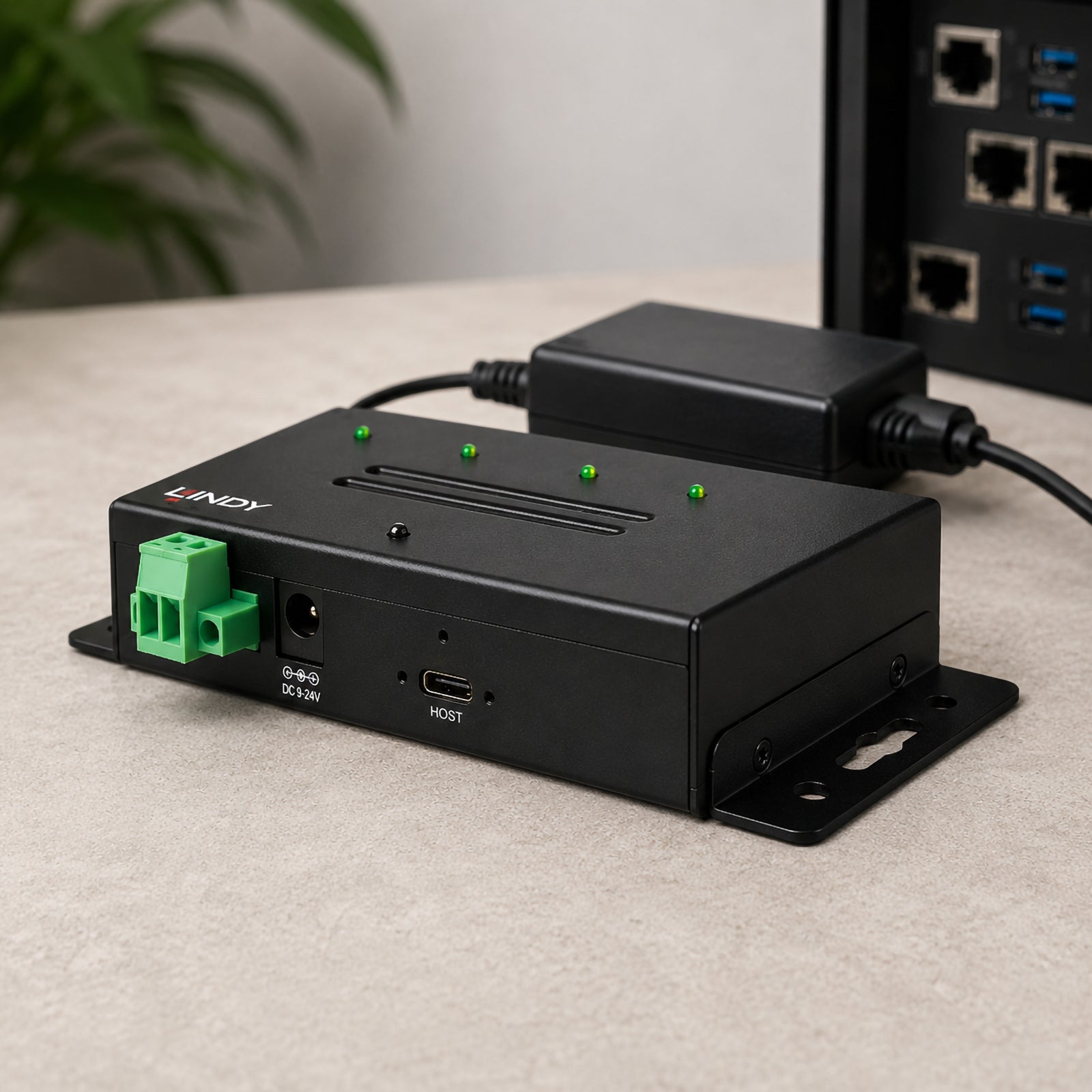 Rear angled close up of the Lindy 4 Port USB 3.2 Gen 2 Industrial Hub showing the USB Type C host connection, DC power socket and industrial terminal block. Positioned beside networking equipment, the image highlights flexible installation options for commercial and industrial environments.