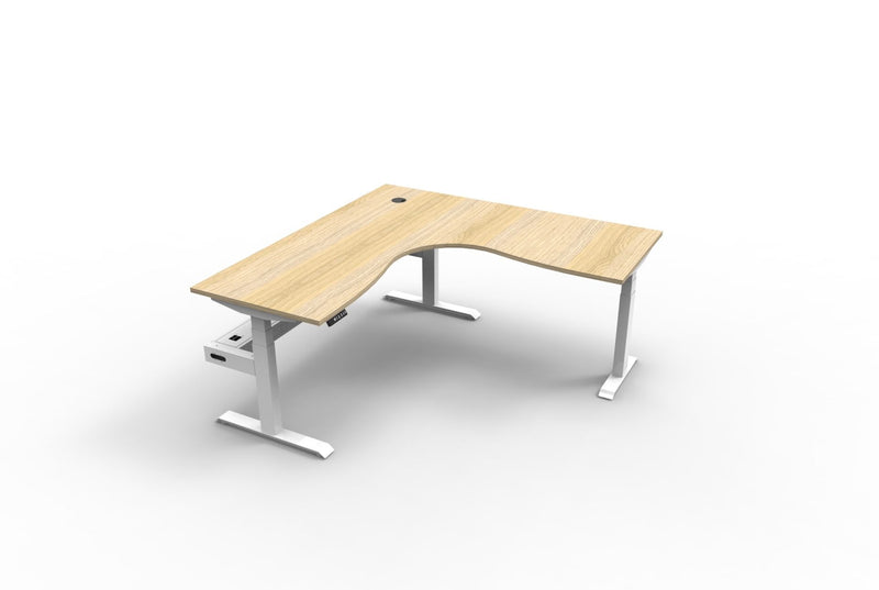 Rapidline Boost+ corner sit stand workstation, Natural Oak top on white triple motor frame and cable tray underneath, front three-quarter view