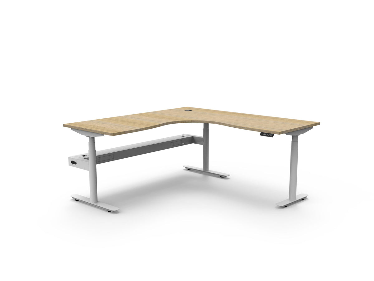 Rapidline Halo Plus electric height adjustable corner workstation on 70mm diameter round columns, E0 rated Natural Oak top with a white satin powdercoated frame, fitted ducted cable tray. Supplied product image for model H+CNRCT1P1818 NO/WS.